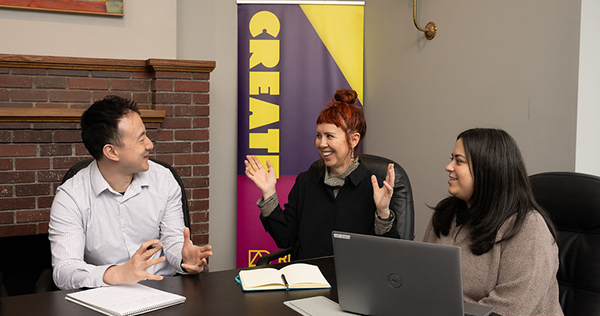 An Asian man and Latina woman speak with a red-headed nonprofit board member in front of a sign that says "Create"
